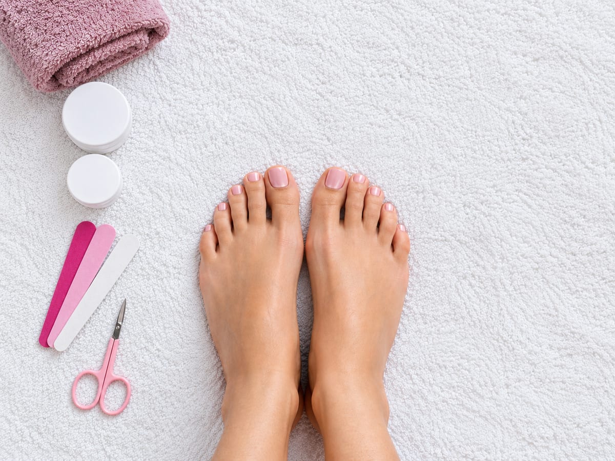 Pies descansando sobre una toalla rosa con herramientas de manicura